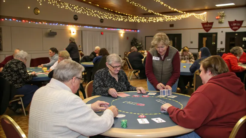 Volunteers and community members gathered around a poker table at a charity casino fundraising night in a New Hampshire community hall